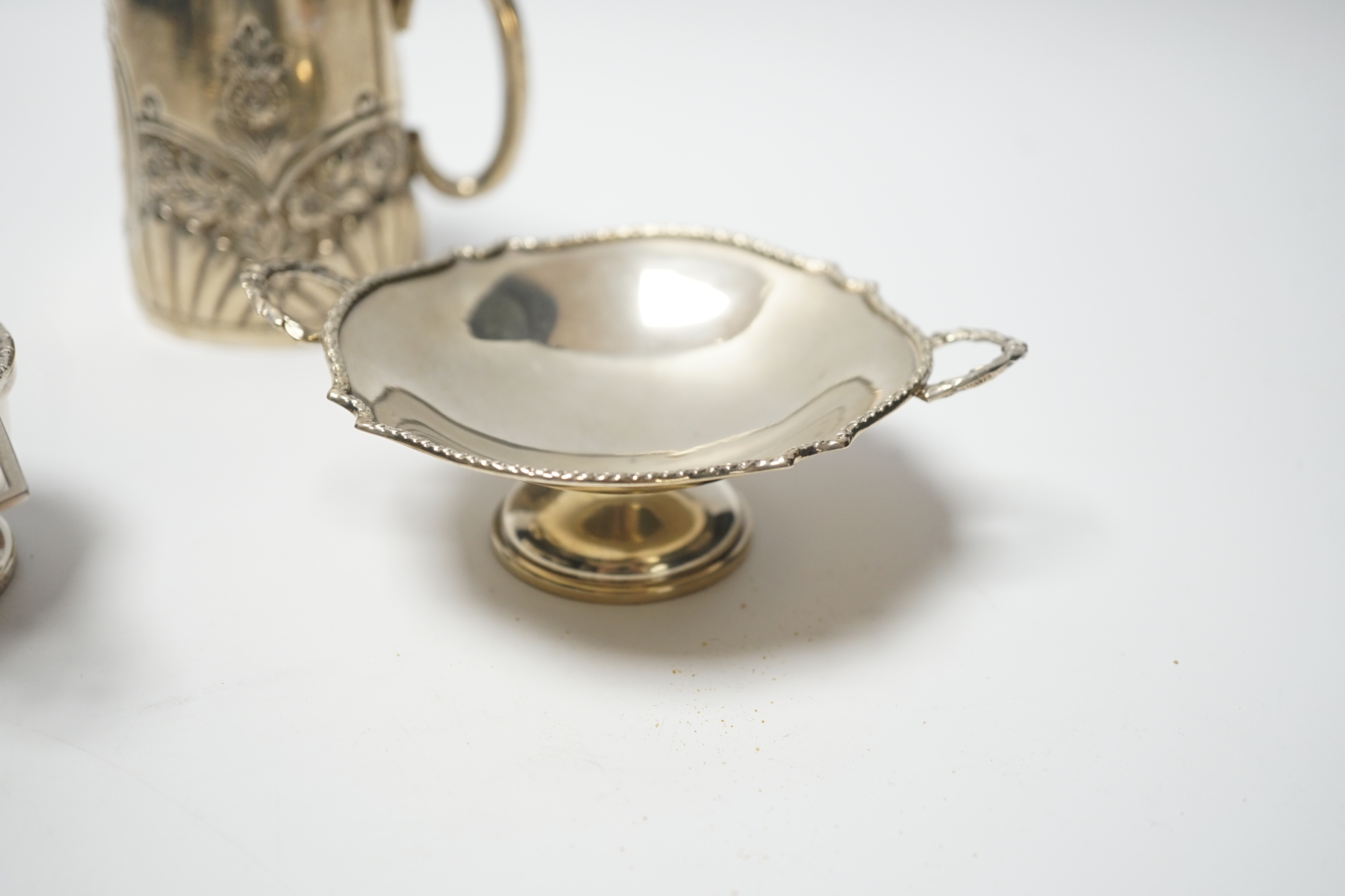 An Edwardian embossed silver christening mug, Birmingham, 1903, height 8cm, together with a silver tea strainer on stand and a small silver two handled dish, 6.9oz.